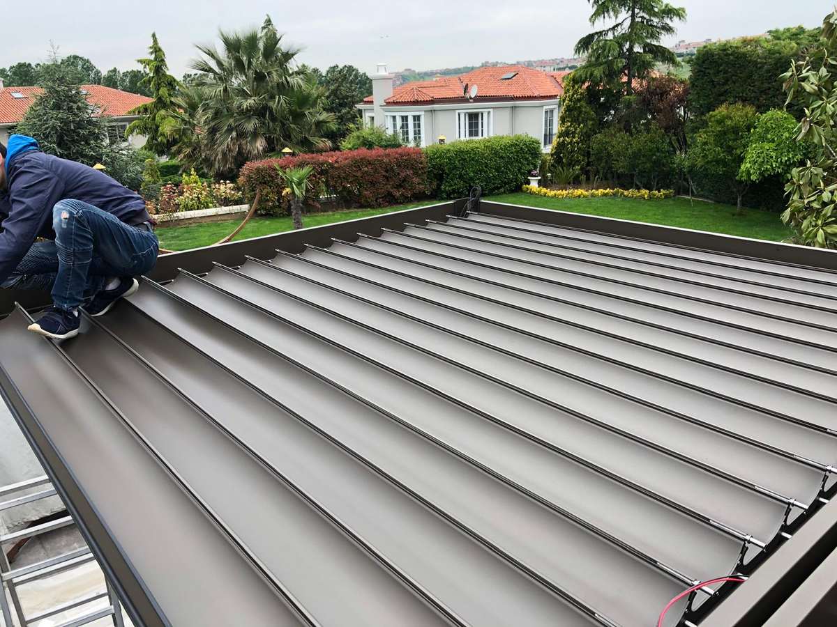 Bioklimatik pergola çatısının montaj sırasında üstten görünümü; ekip üyesi antrasit lamelleri yerleştiriyor