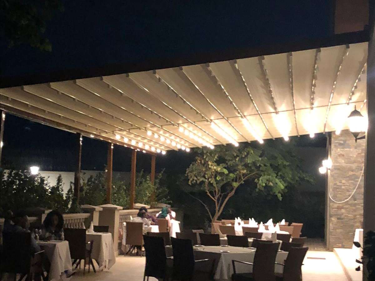 Akşam saatinde restoran terasını örten LED aydınlatmalı beyaz alüminyum pergola